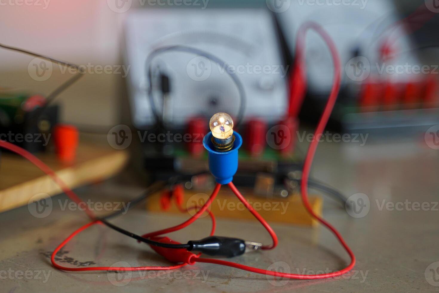 Close-up of a simple electrical circuit with a lit light bulb and red wires on a workbench. Physics, science education, and experiment. photo