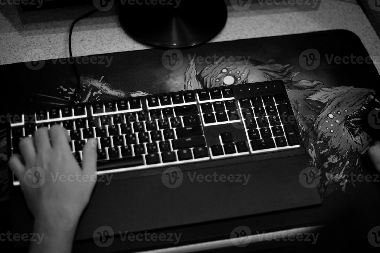 Black and white overhead view of keyboard with hand on WASD keys. Gaming mousepad on desk, moody atmosphere representing gaming addiction, frustration or negative aspects of games photo