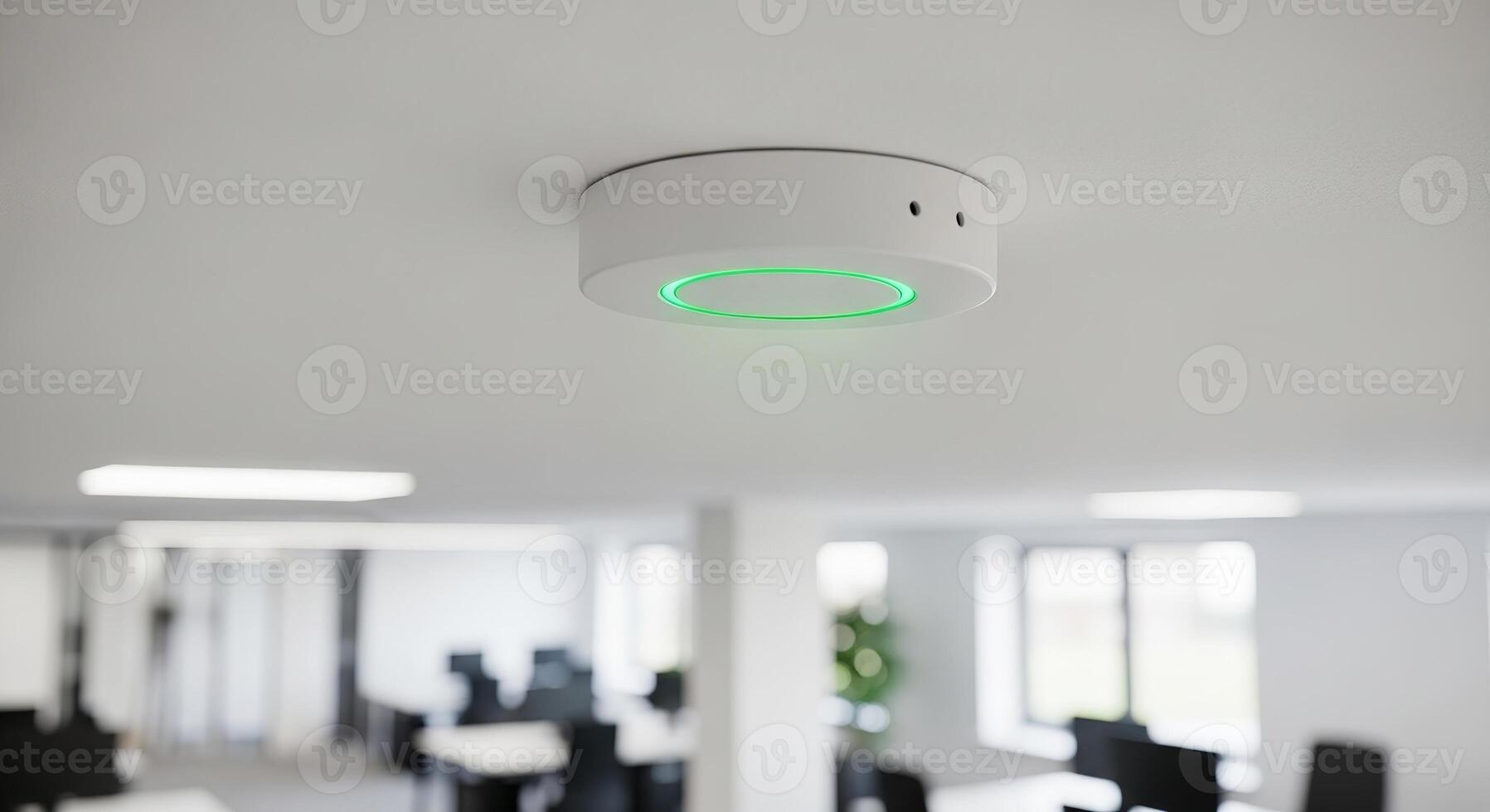 A white ceiling mounted device with a glowing green ring in an office setting is visible now photo