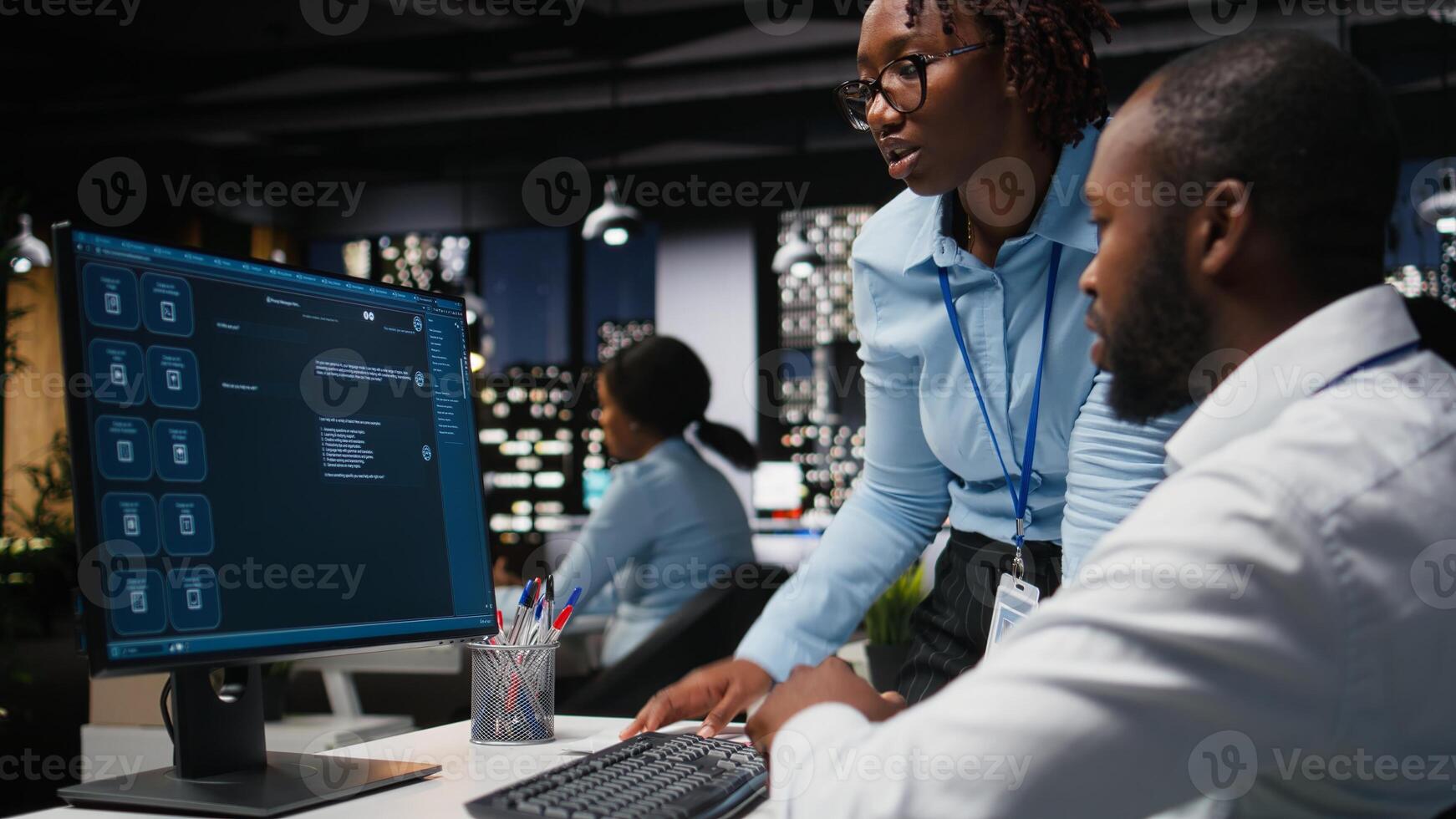 Two black workers interacting with a virtual assistant on computer at desk, responses and smart automation to improve online communication. Data driven AI solutions. photo