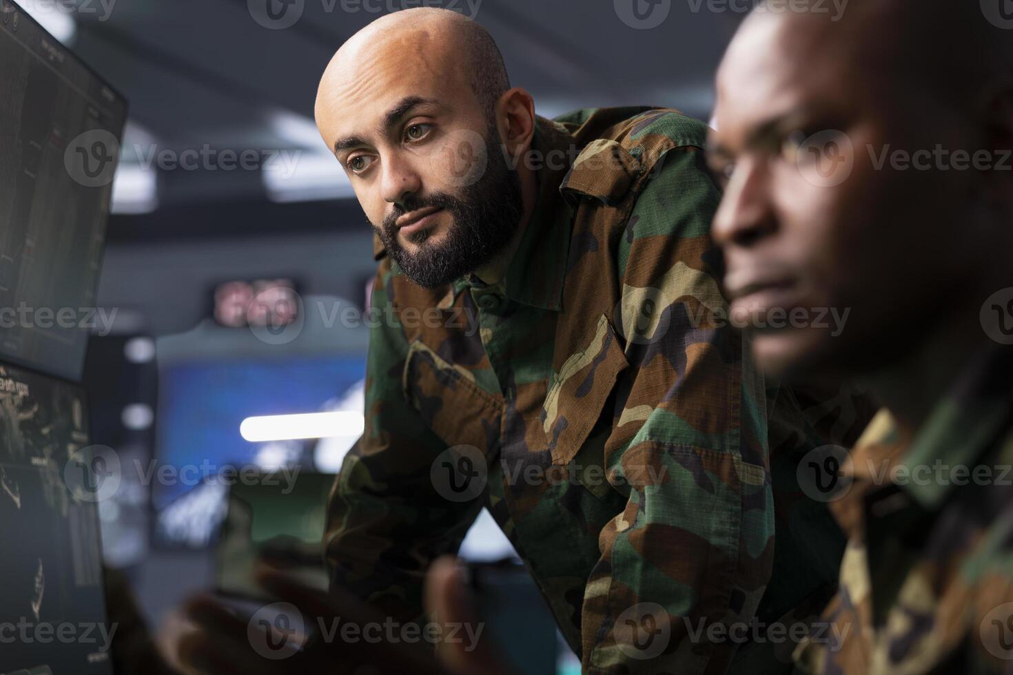 Team of military dispatchers looking at surveillance monitor, analyzing data to allocate resources to units based on mission needs. Agent and colleague examining strategic data on equipment displays photo