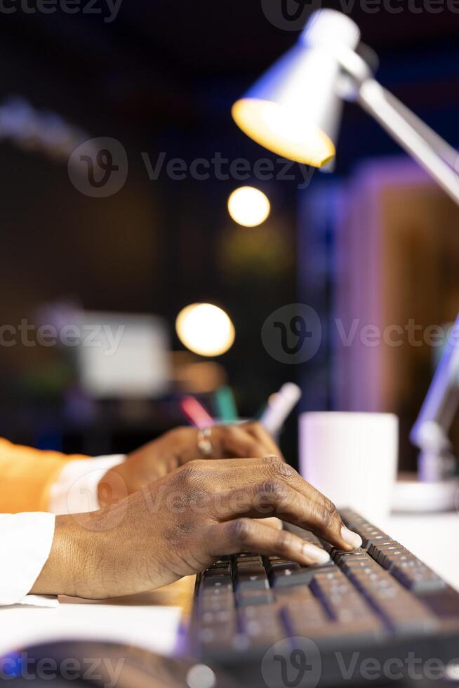 Hardworking freelancer typing on laptop keyboard in home office to solve various work tasks. Close up of teleworker at desk typing on notebook to finish project paperwork photo