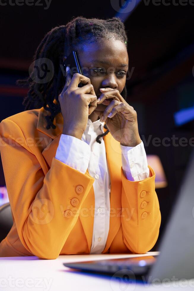 Woman seated at home office desk using laptop, answering phone call while checking emails displayed on screen. Remote worker in telephone call with friend while reading messages in inbox photo