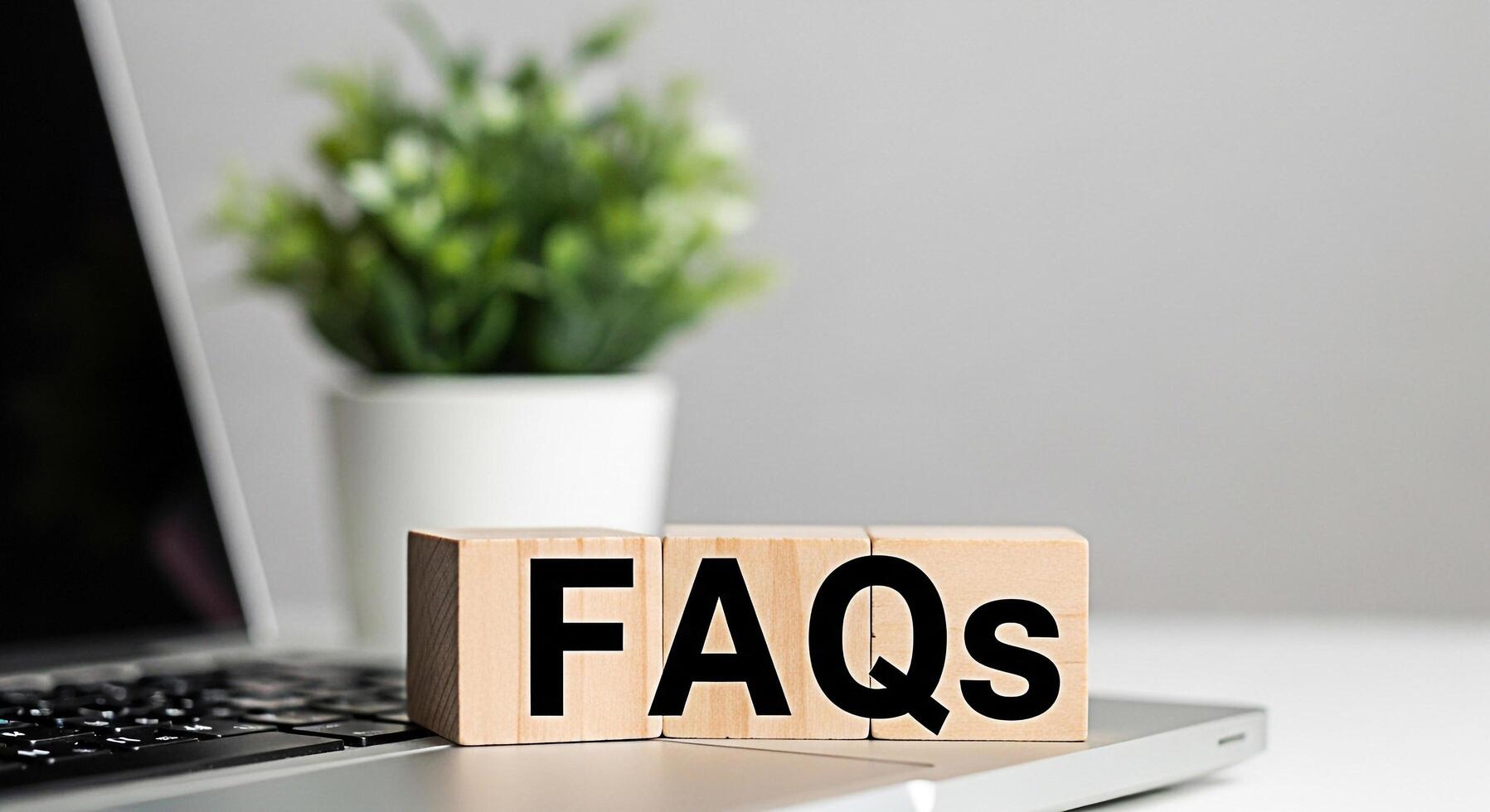 Wooden blocks displaying FAQs on a laptop in a bright modern office setting symbolizing readily available information and customer support for online queries and common questions photo