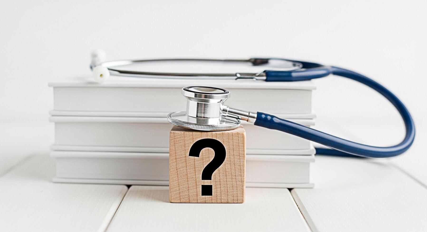Stethoscope resting on a question mark block placed on top of a stack of books on a white wooden table symbolizing medical uncertainty and the search for answers in healthcare creating a thoughtful mo photo
