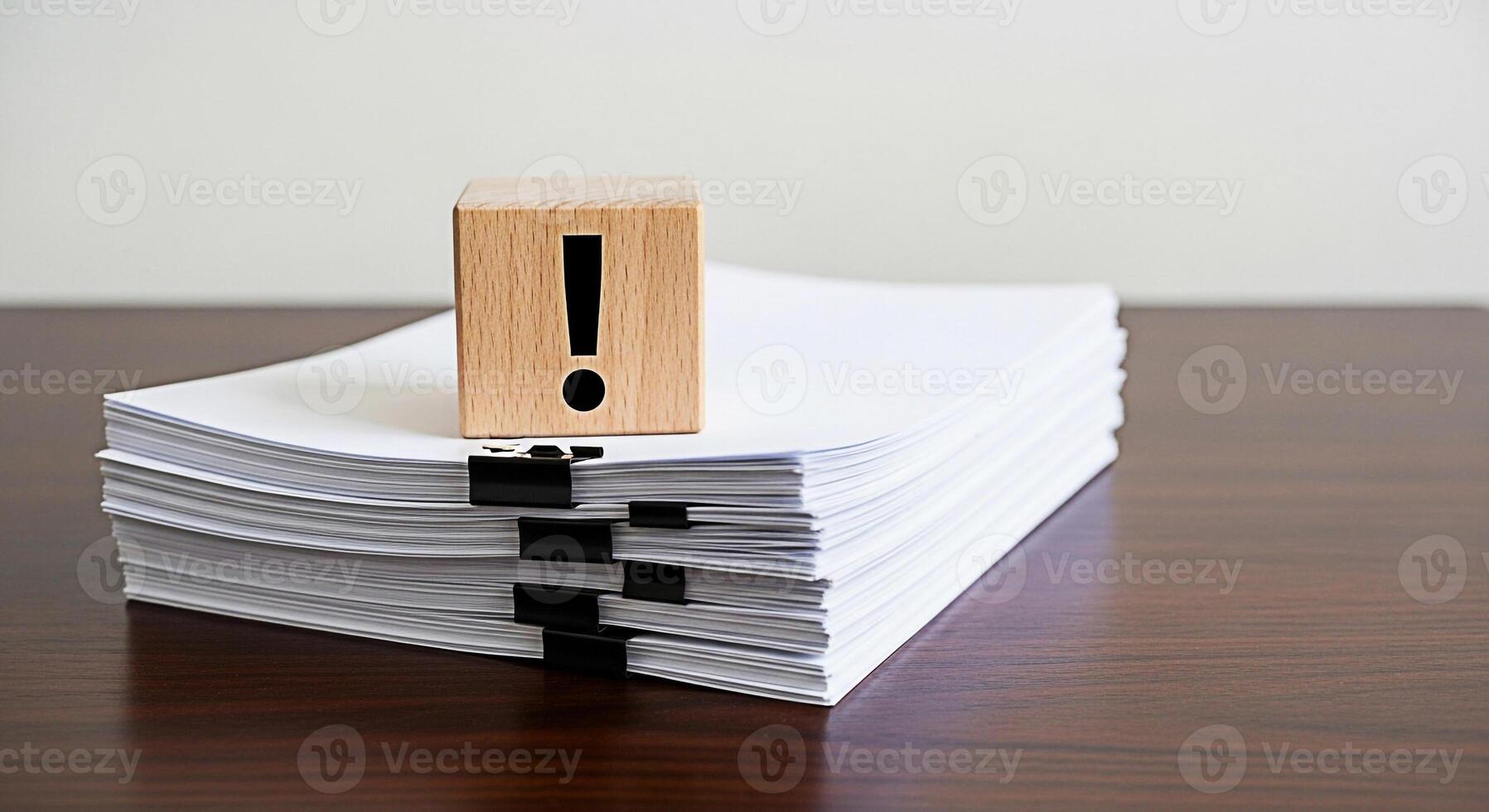 Urgent documents A wooden block with an exclamation mark sits atop a stack of papers secured with binder clips on a dark wooden desk symbolizing important tasks and deadlines in a busy office environm photo