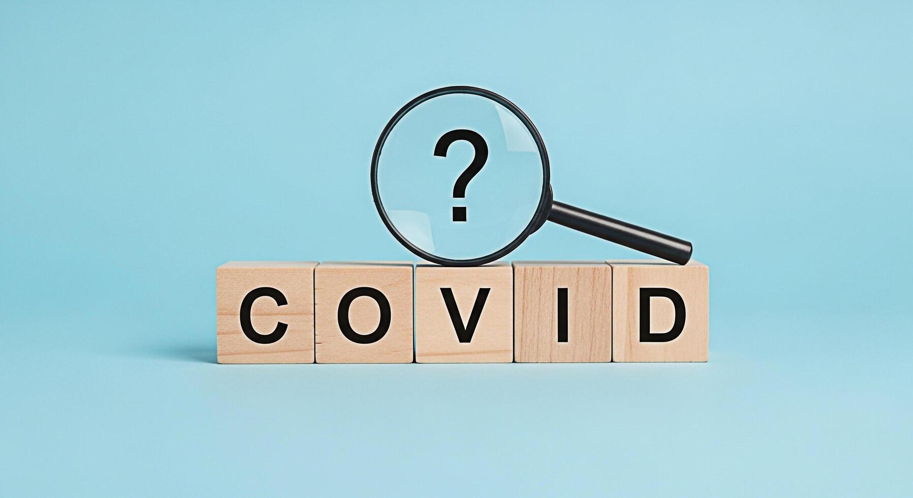 Magnifying glass hovering over wooden blocks spelling COVID with a question mark symbolizing uncertainty and the ongoing search for answers in a light blue studio setting creating a sense of concern photo