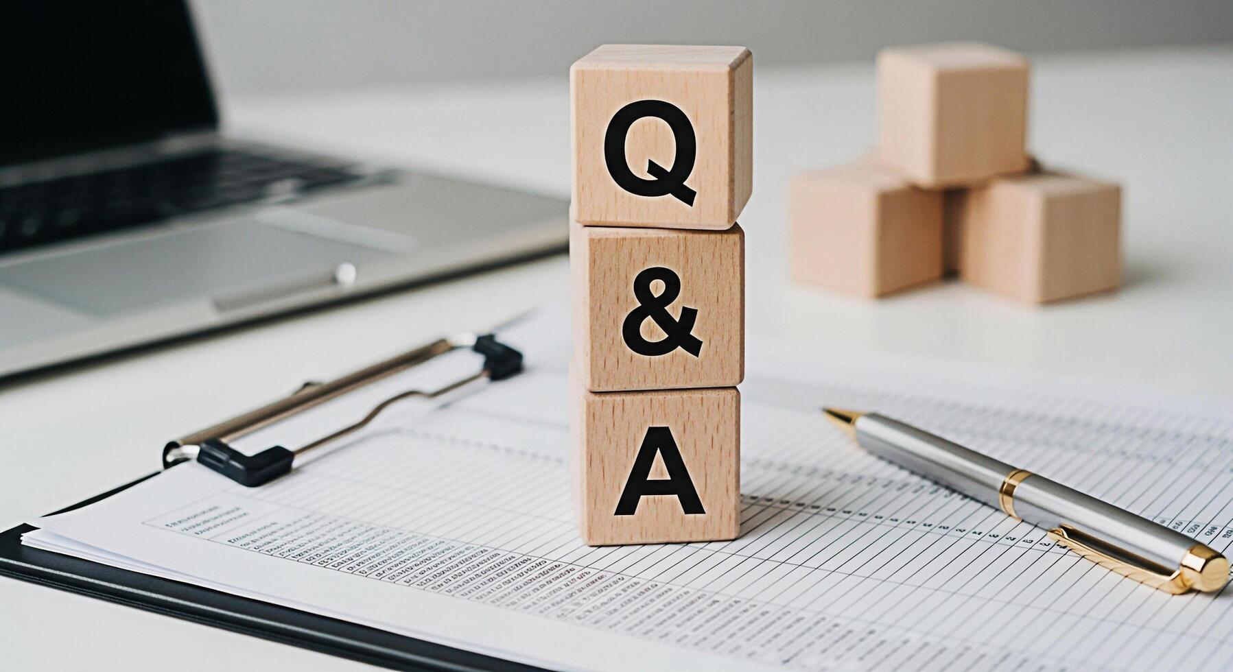 Wooden blocks displaying QA on a bright white desk with a laptop clipboard and pen representing information support and answers to questions in a professional and informative setting photo