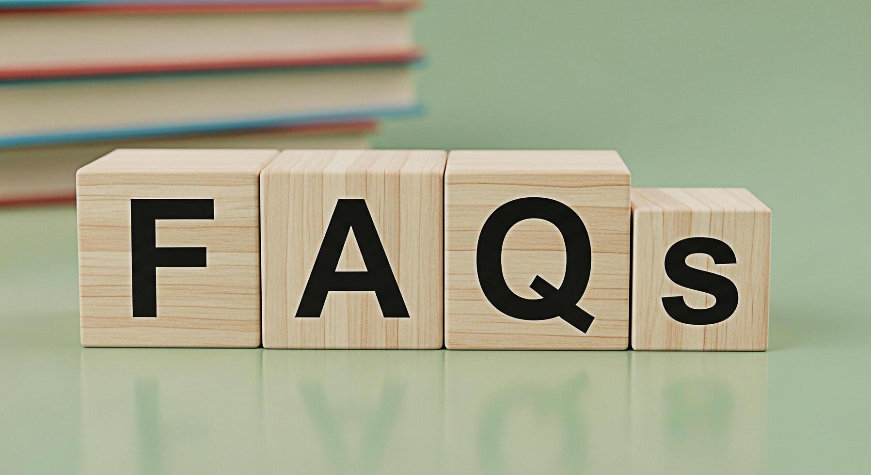 Wooden blocks spelling FAQs resting on a green surface with blurred books in the background representing information help and frequently asked questions for customer support and online resources photo