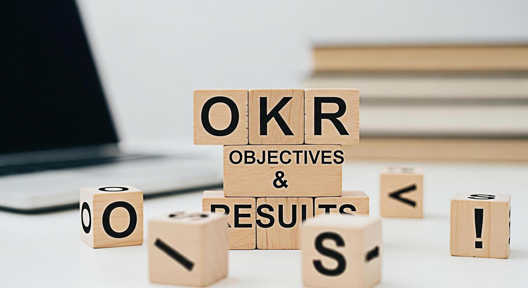 Wooden blocks spelling OKR Objectives and Key Results on a white desk with a laptop and books representing business strategy goal setting and performance management in a modern office environment photo
