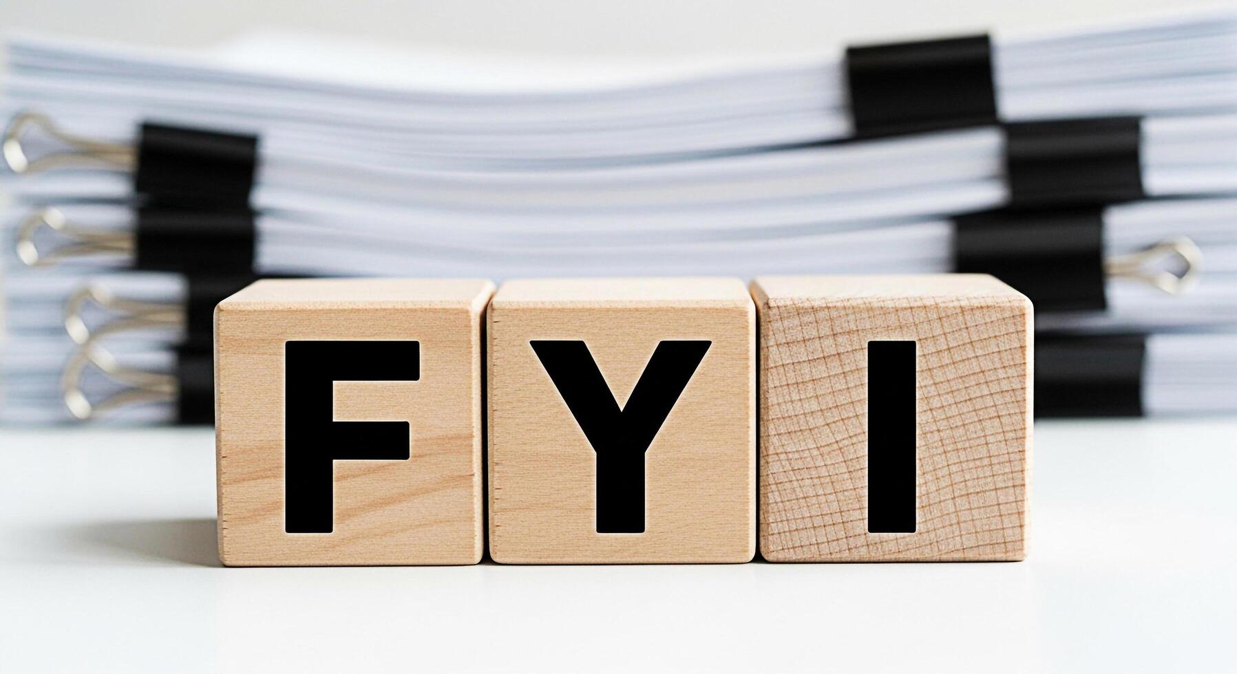 Wooden blocks displaying FYI on a white surface with a stack of documents in the background conveying a message of important information and awareness in a professional setting photo