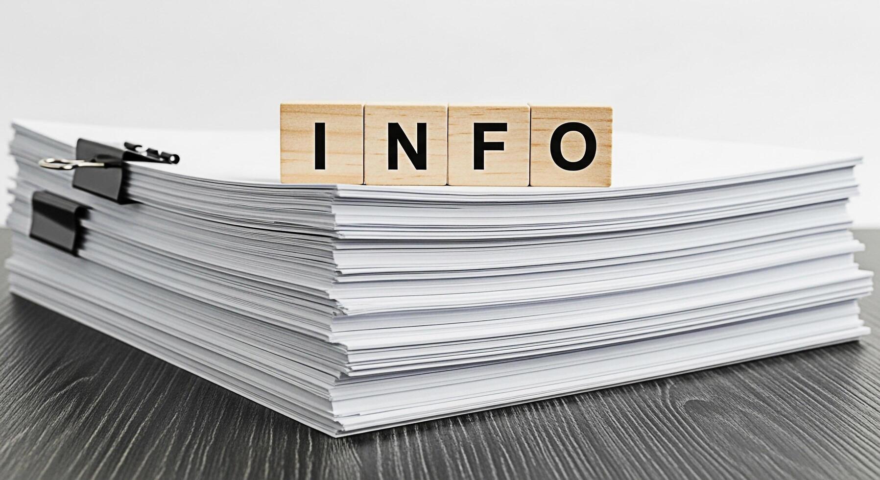 Stack of white papers displaying wooden blocks spelling INFO on a dark wooden desk representing data overload and the need for information management in a modern office environment photo