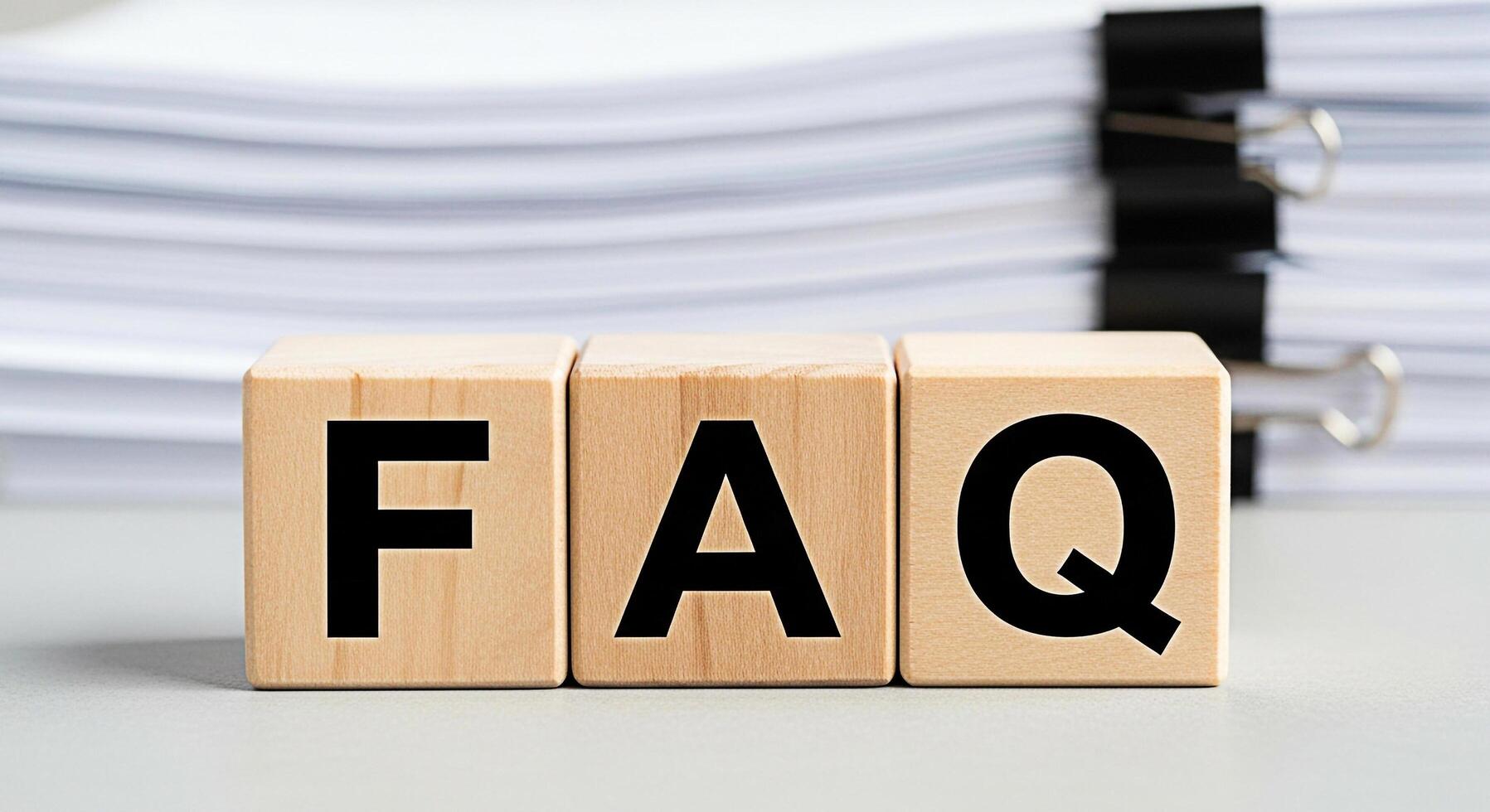 Wooden blocks displaying FAQ in front of a stack of documents representing frequently asked questions and providing helpful information in a business or educational setting conveying clarity and guida photo