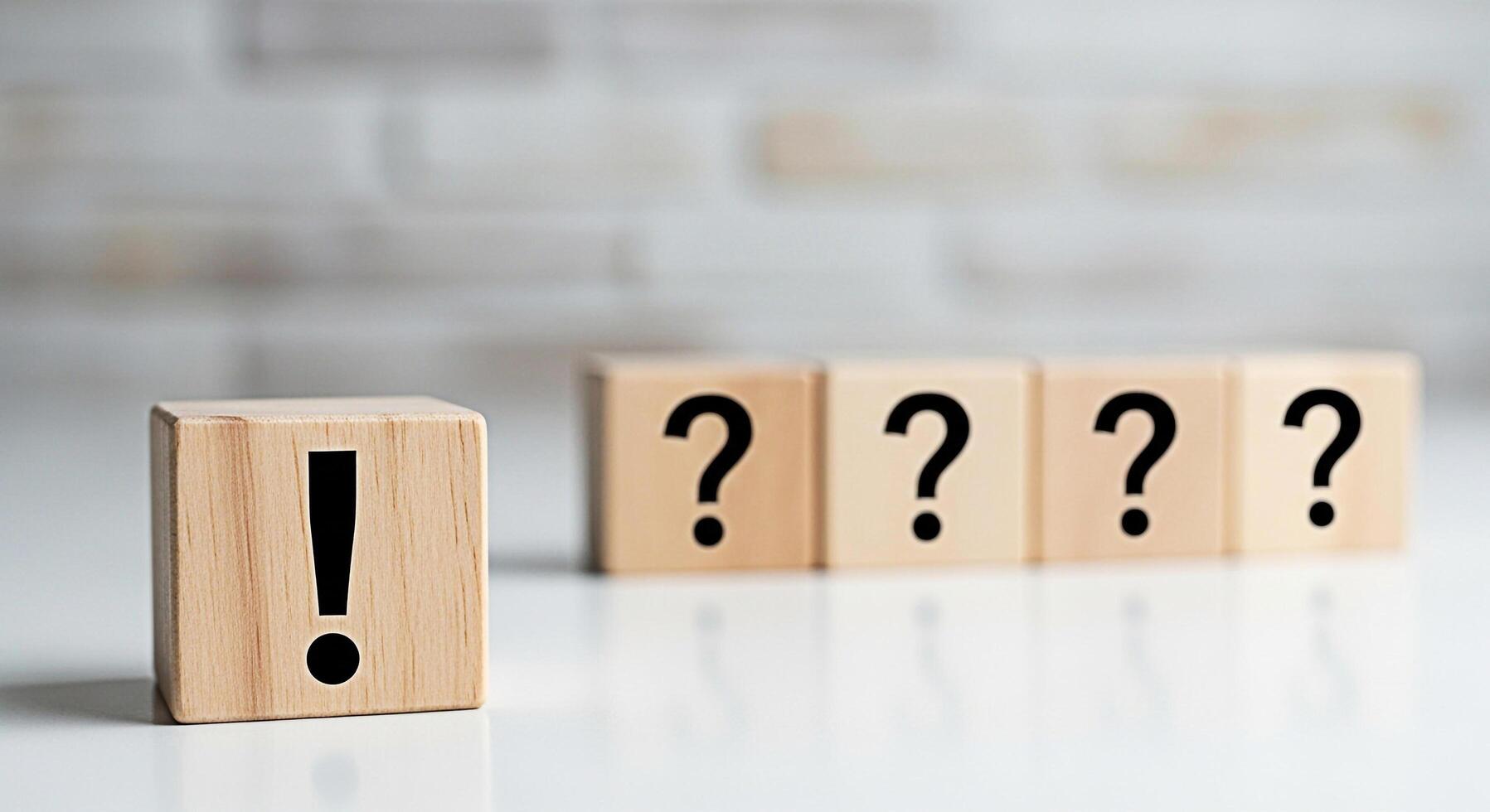 Wooden blocks displaying an exclamation mark stands out from the question marks on a white table against a blurred brick wall symbolizing solutions answers and problemsolving in a bright and clean set photo