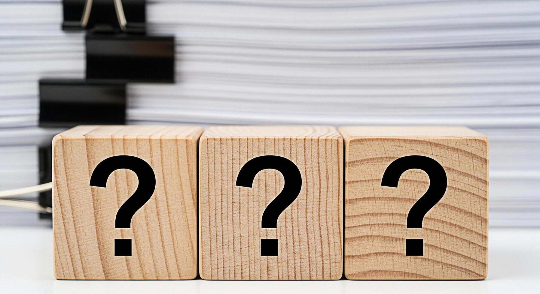 Three wooden blocks displaying question marks in a bright studio setting symbolizing uncertainty and the need for answers amidst a stack of documents creating a sense of inquiry and problemsolving photo