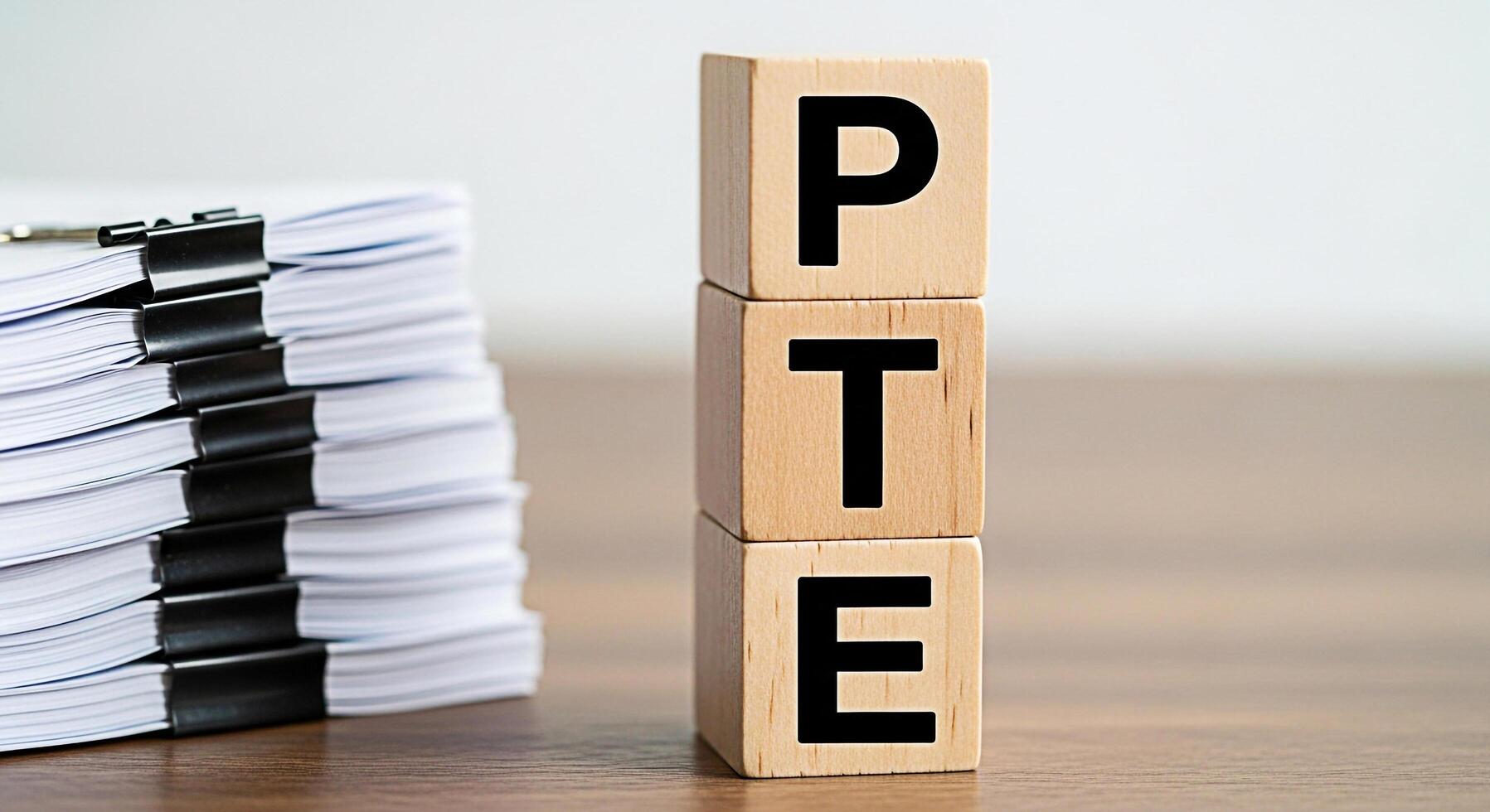 Wooden blocks spelling PTE next to a stack of documents on a wooden desk representing the Pearson Test of English Academic exam preparation and the importance of paperwork and documentation photo