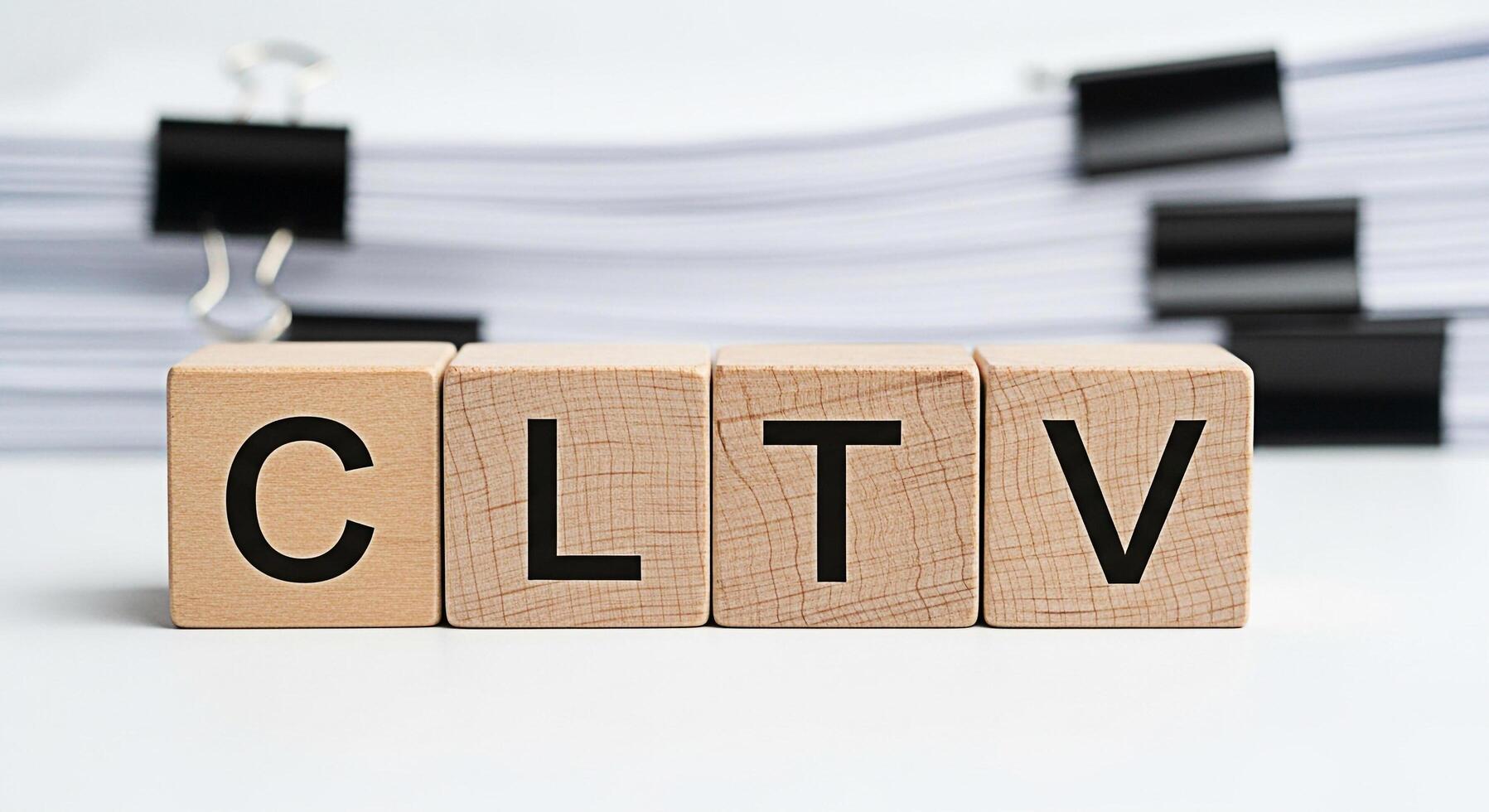 Wooden blocks spelling out CLTV on a white surface with blurred documents and binder clips representing customer lifetime value and business analytics in a clean professional setting photo