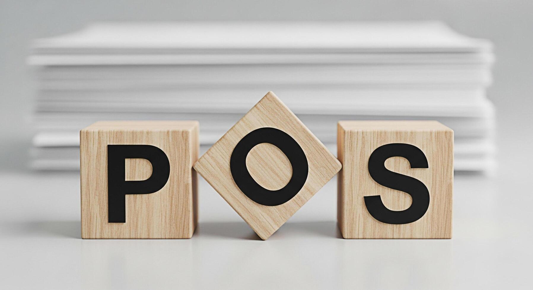 Wooden blocks displaying POS on a white surface with a stack of papers in the background representing point of sale systems and retail technology in a clean and modern setting photo