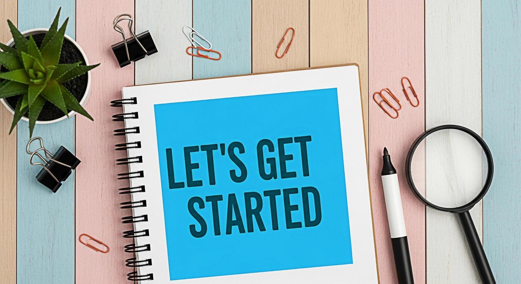 Overhead shot of a notebook displaying Lets Get Started on a colorful wooden desk surrounded by office supplies creating a motivational and organized workspace atmosphere photo