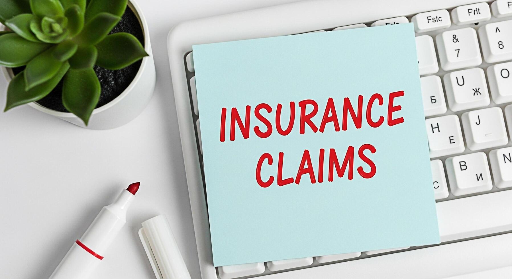 Closeup of a note with Insurance Claims written on it placed on a white computer keyboard in a bright office setting representing financial security and the process of filing for coverage photo