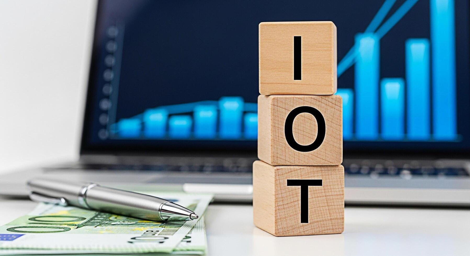 Wooden blocks spelling IOT placed on a desk with Euro banknotes and a pen in front of a laptop displaying a rising graph representing the Internet of Things and financial growth in a modern business s photo
