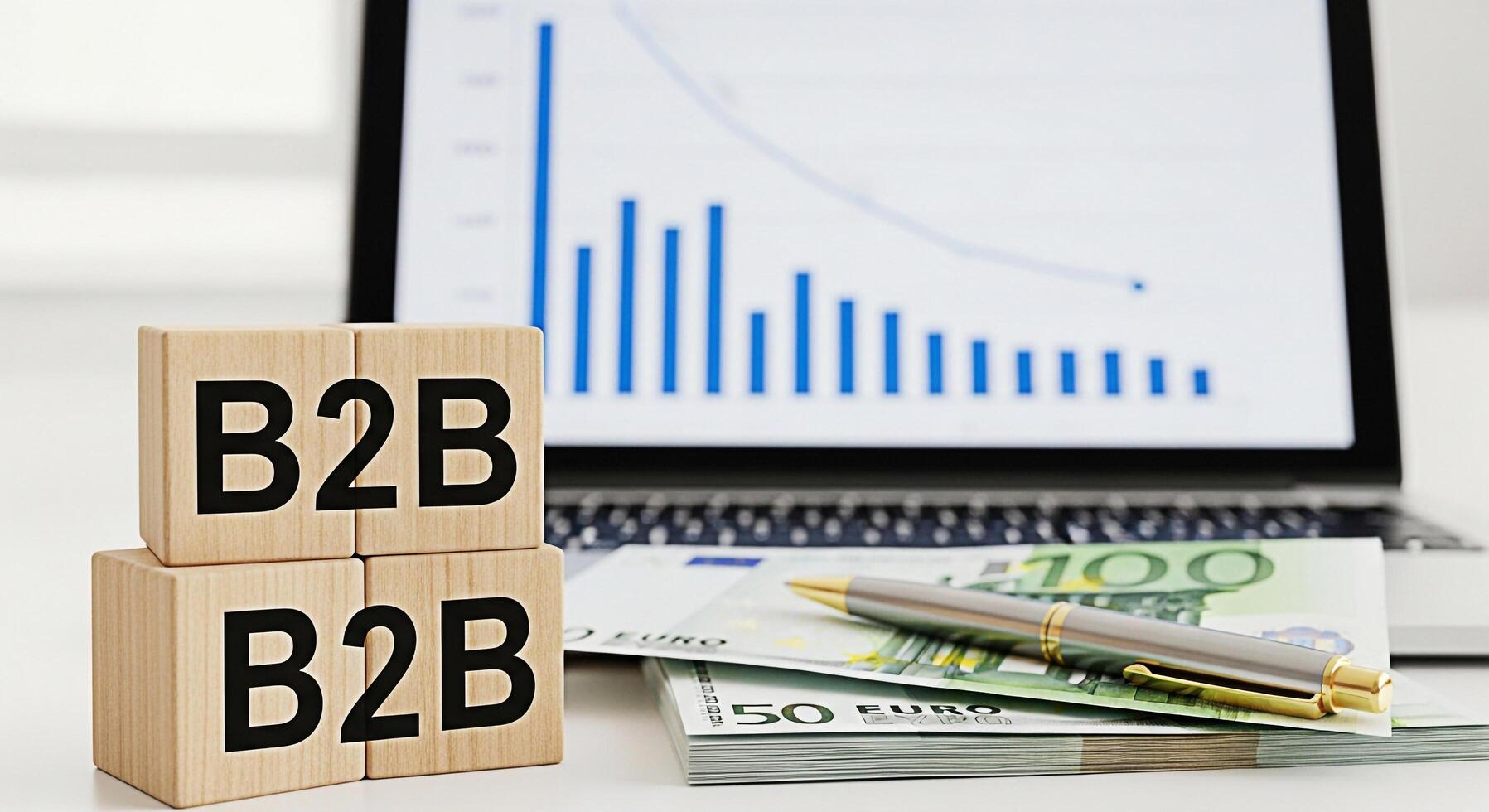Wooden blocks displaying B2B on a white desk with a laptop showing a declining graph and Euro banknotes representing business to business transactions and financial challenges in a modern setting photo