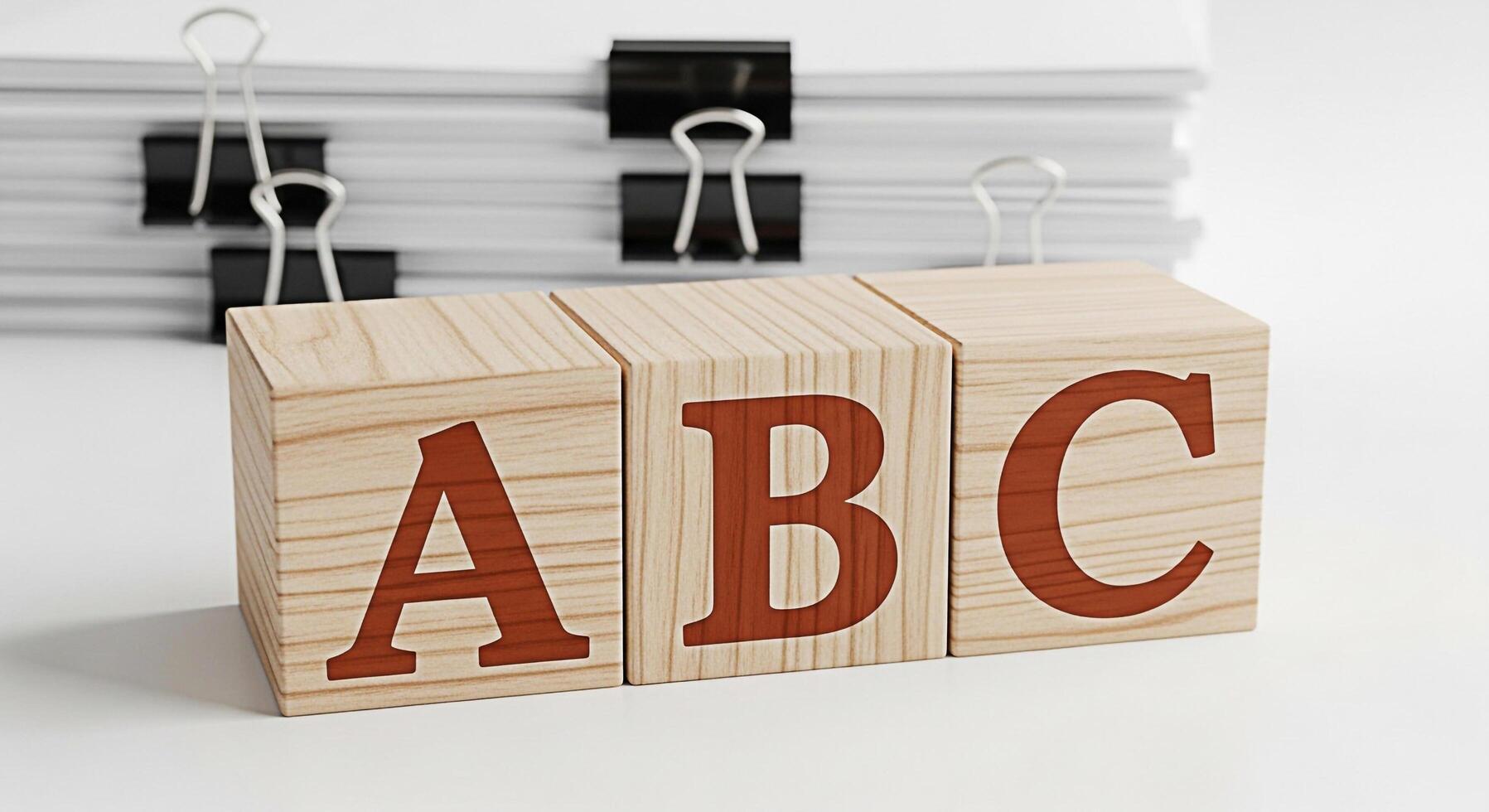Wooden ABC blocks sitting on a white desk with a stack of papers and binder clips in the background representing the basics of education and learning in a clean and organized environment photo