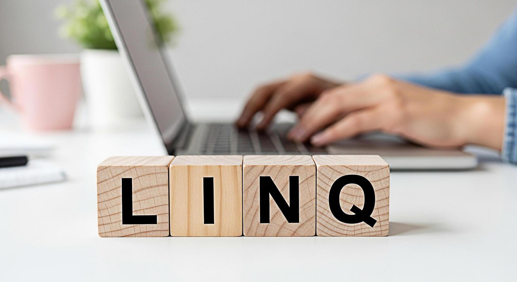 Person typing on a laptop behind wooden blocks spelling LINQ on a white desk in a bright office conveying connection and technology in a modern workplace ideal for business and innovation concepts photo