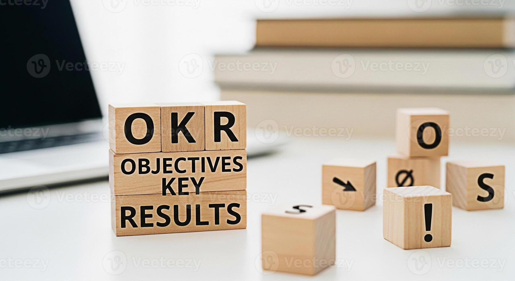 Wooden blocks displaying OKR Objectives Key Results on a white desk with a laptop and books symbolizing business strategy and goal setting in a modern office environment fostering a sense of focus and photo