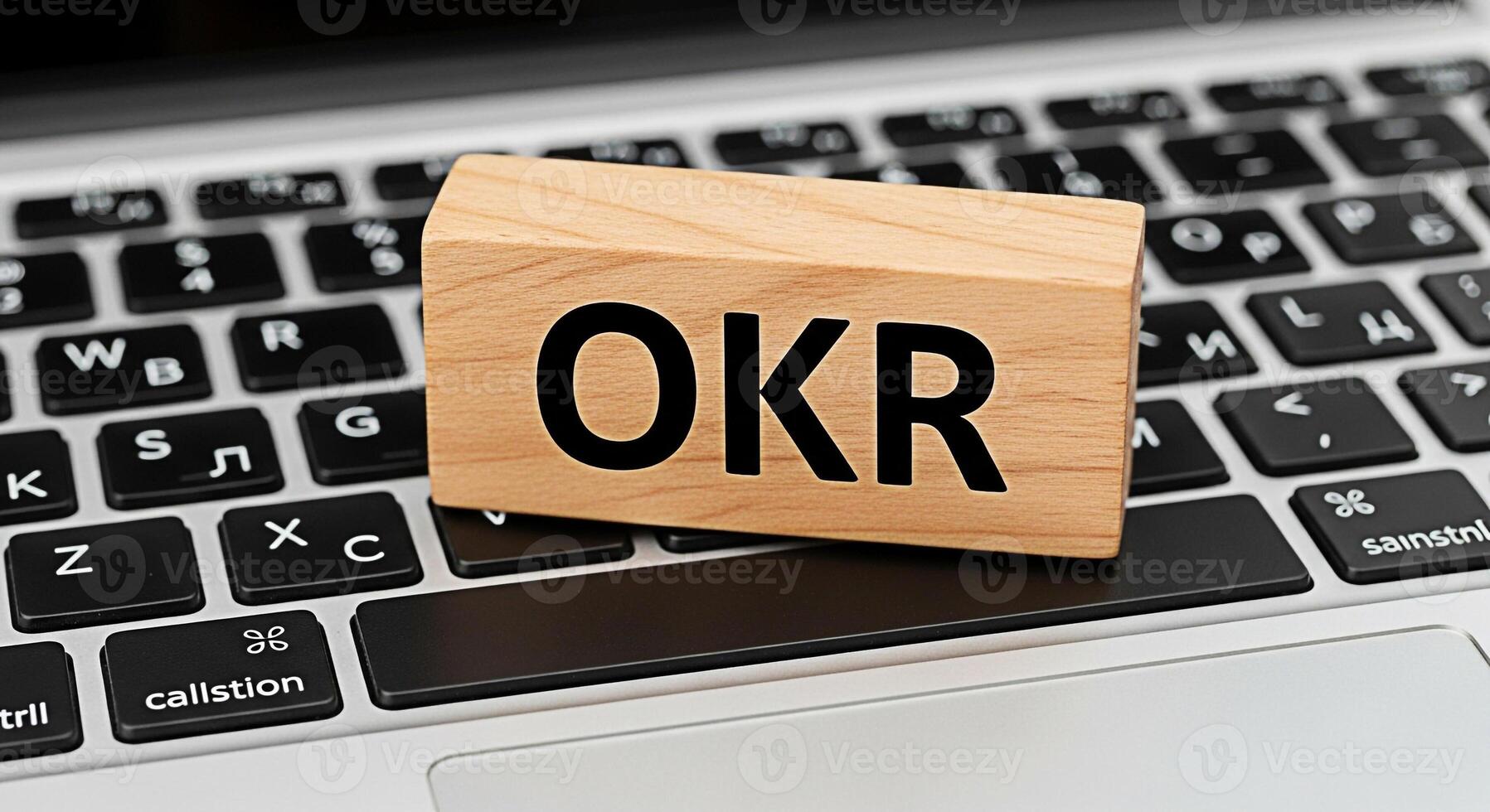 Wooden block displaying OKR on a laptop keyboard representing objectives and key results in a modern office setting symbolizing goal setting and business strategy for increased productivity photo