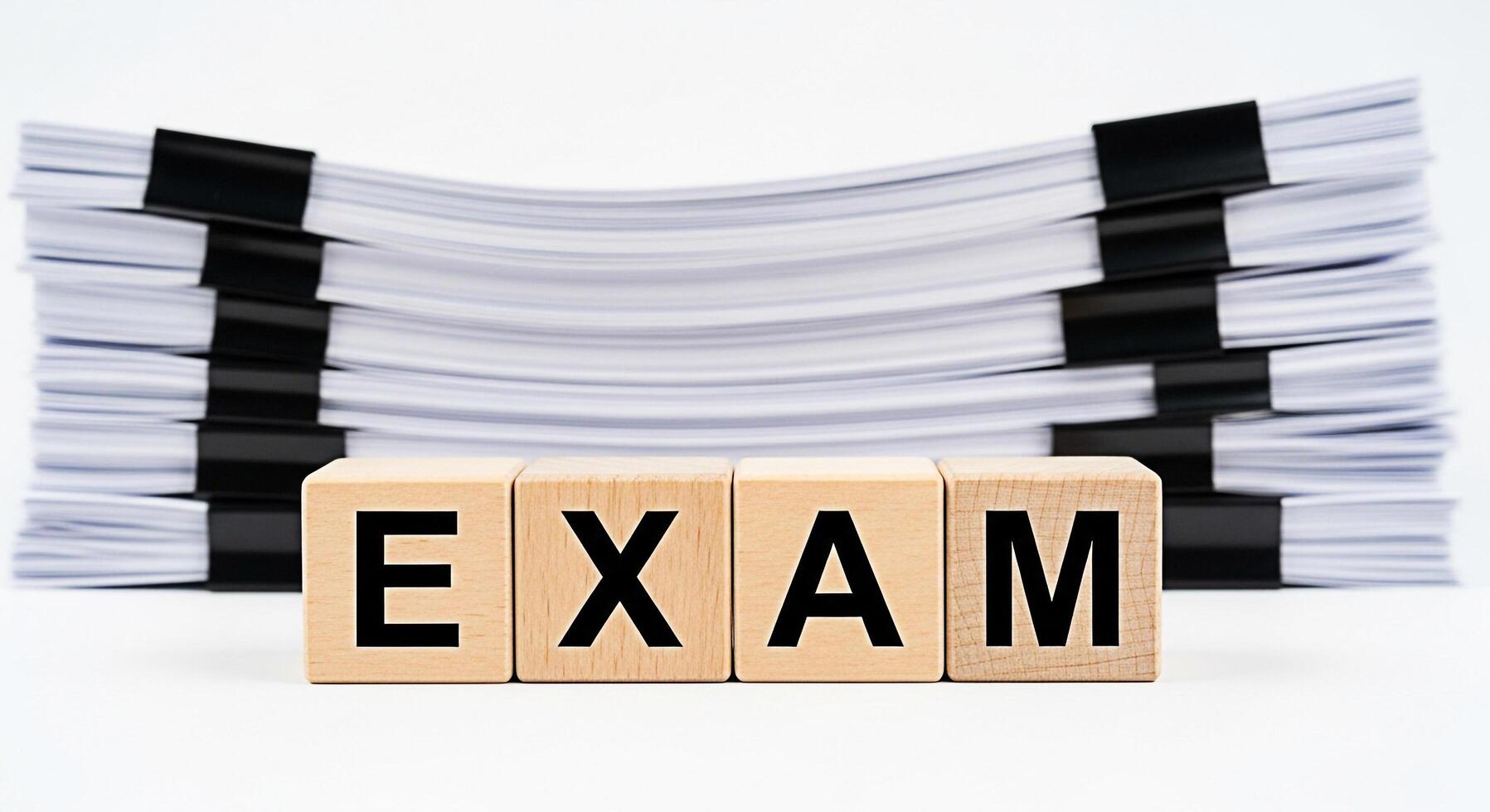 Wooden blocks spelling EXAM in a bright studio setting with a stack of papers symbolizing the pressure and preparation required for academic success and the importance of education photo