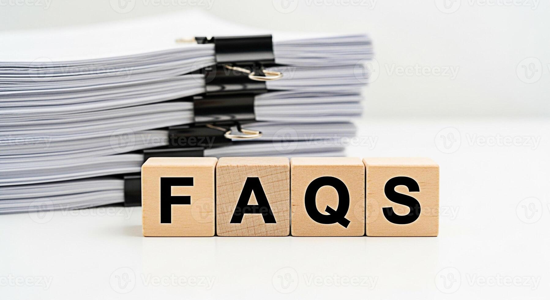 Stack of documents with wooden blocks spelling FAQs on a white desk representing frequently asked questions and information resources in a clean and organized office environment photo
