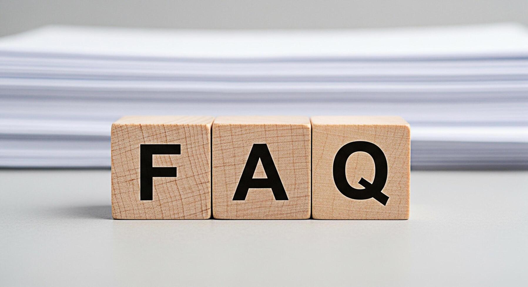 Wooden blocks displaying FAQ on a neutral surface with stacked papers in the background representing frequently asked questions and information resources in a clear and accessible manner photo