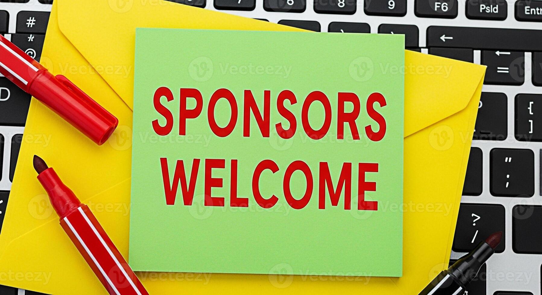 Bright green note on a keyboard displaying Sponsors Welcome with colorful markers and a yellow envelope creating an inviting and supportive atmosphere for potential partners and contributors photo