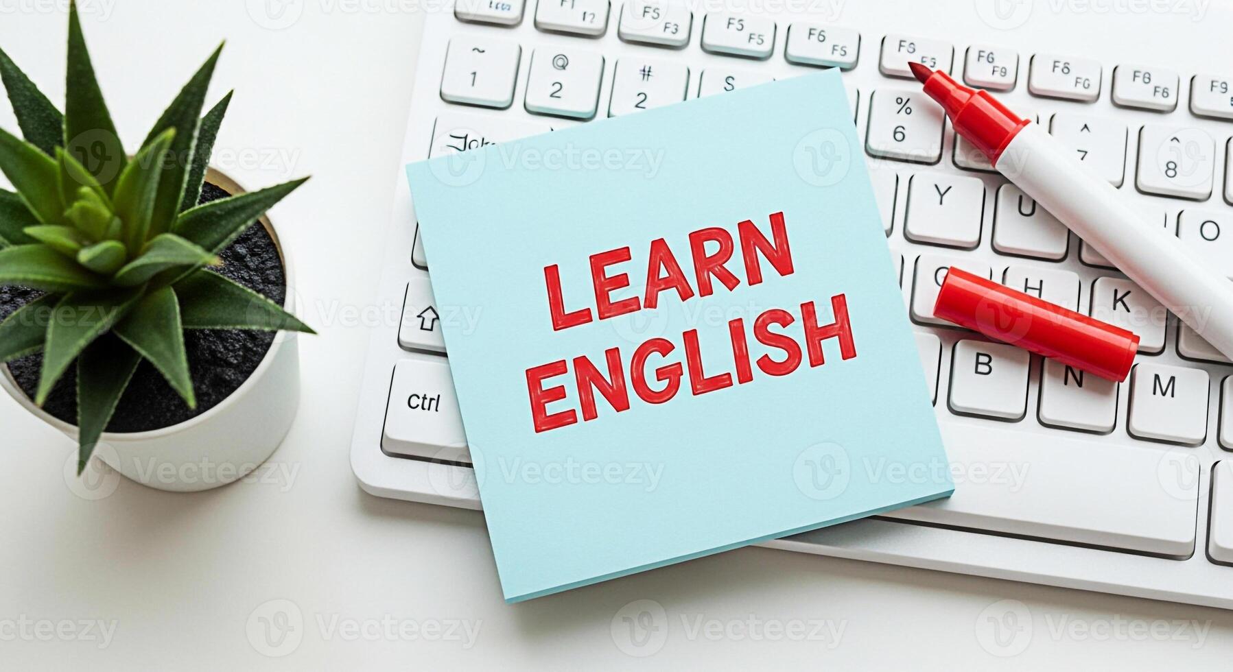 Light blue sticky note with the words Learn English in red resting on a white keyboard with a red marker and a small green potted plant conveying a sense of education and language acquisition photo