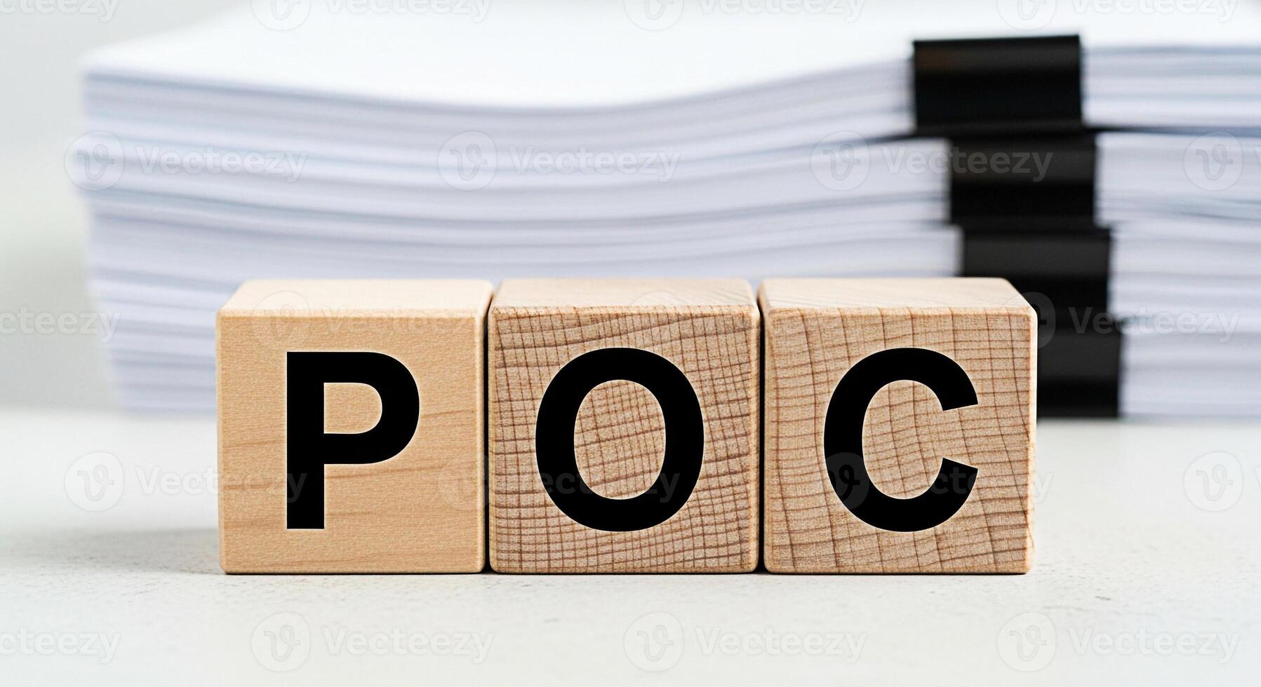 Wooden blocks displaying POC on a white table with a stack of papers in the background representing proof of concept and the importance of documentation in business and project management photo