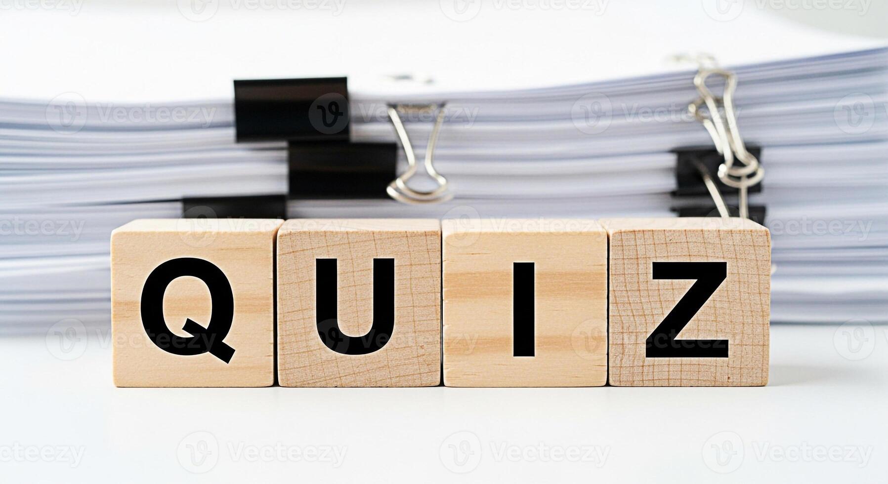Wooden blocks spelling QUIZ in a bright studio setting representing knowledge assessment and learning with a stack of papers in the background creating a concept of education and examination photo