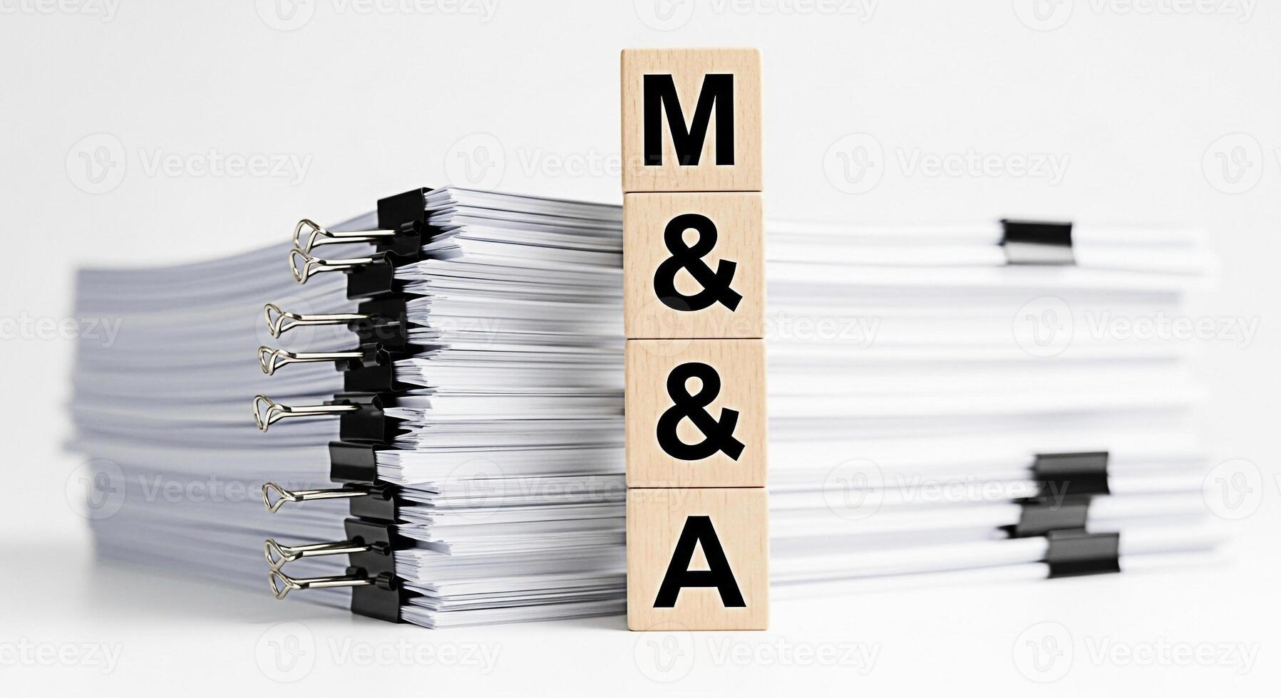 Wooden blocks spelling MA standing next to large stacks of documents on a white surface representing mergers and acquisitions in a corporate setting conveying a sense of business and legal processes photo
