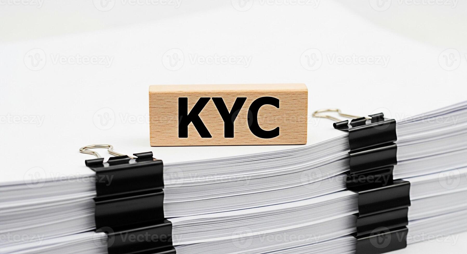 KYC wooden block resting on a stack of documents secured with binder clips in a bright minimalist office setting representing compliance verification and regulatory adherence for financial institution photo