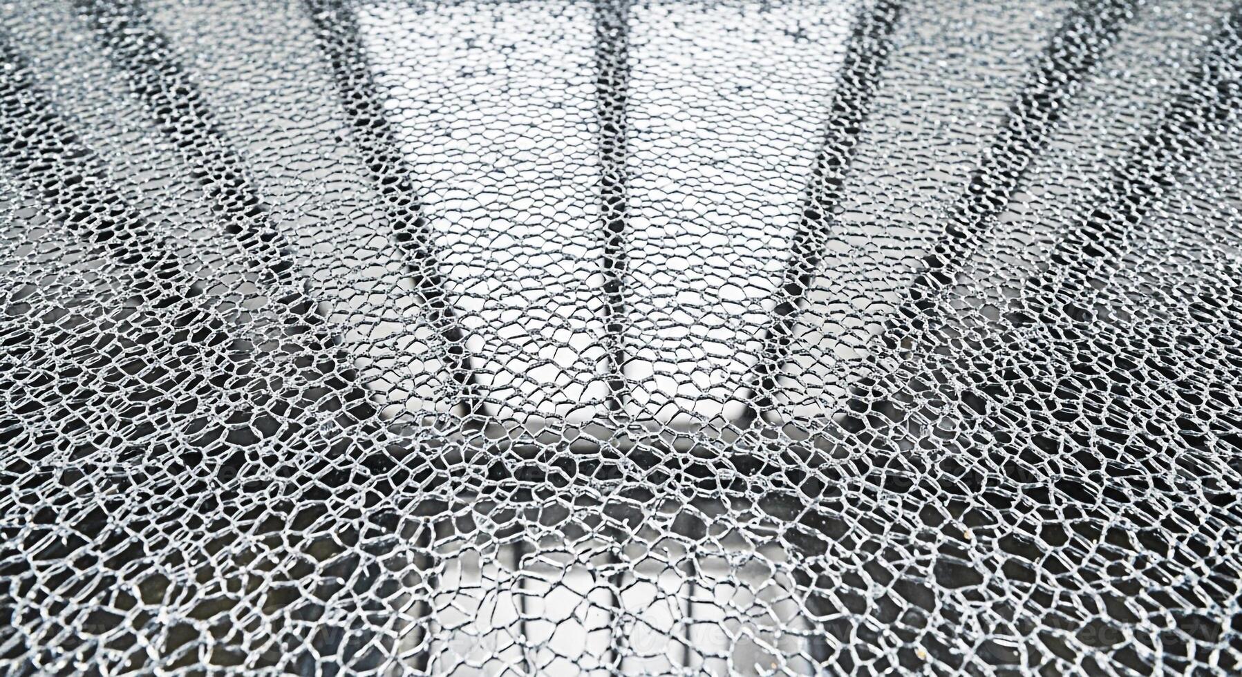 Cracked glass pane displaying intricate fracture patterns in a bright sunlit environment creating a sense of fragility and vulnerability ideal for abstract designs and conceptual backgrounds photo