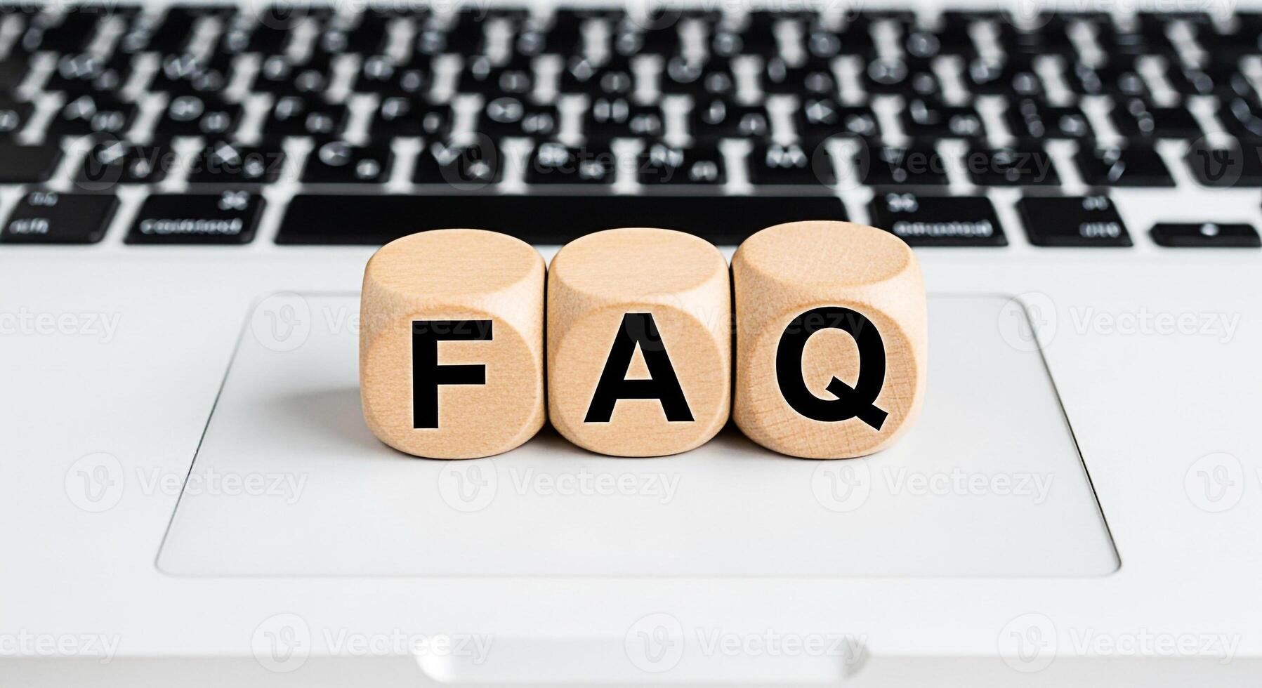 Wooden blocks displaying FAQ on a laptop keyboard representing frequently asked questions and information retrieval in a digital environment conveying clarity and accessibility for online support photo