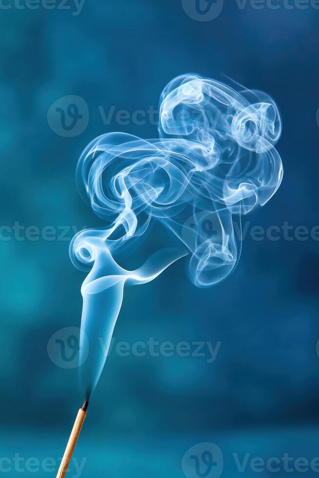Soft incense smoke rising gracefully from a stick, creating ethereal patterns against a blurred blue background, evoking a sense of calm and tranquility with copy space photo