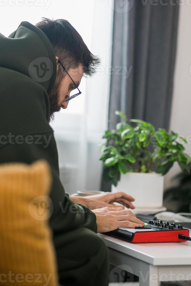 Man recording electronic music track with portable midi keyboard on laptop computer in home studio close-up. Producing and mixing music beat making and arranging audio photo