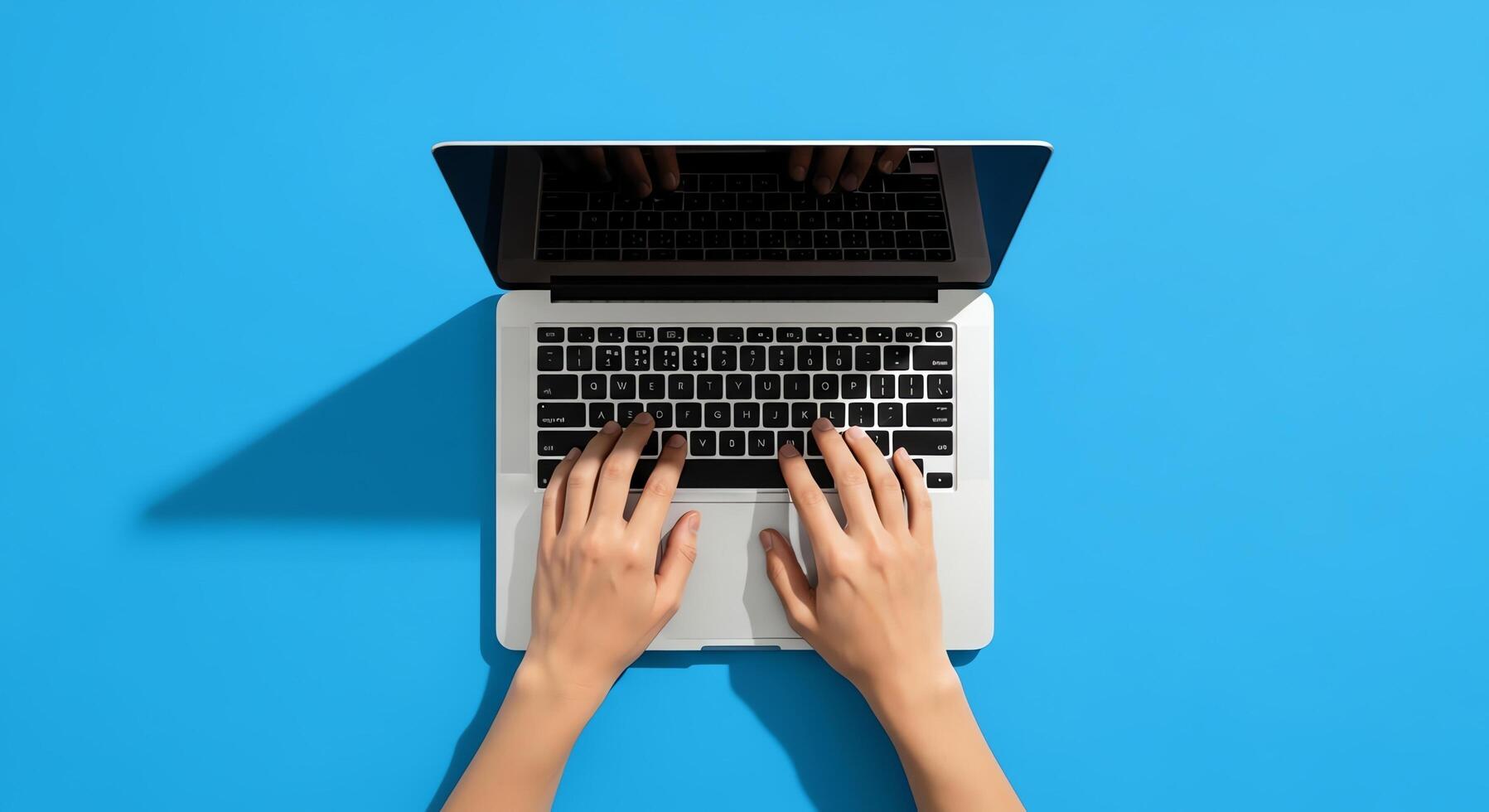 Overhead view of hands typing on a laptop computer on a blue surface photo
