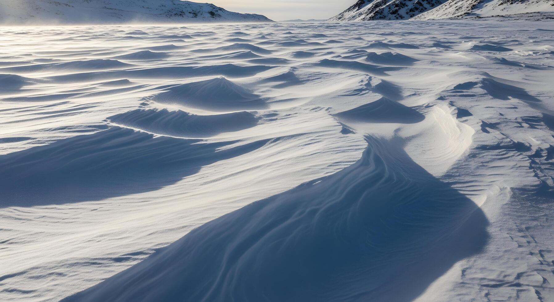 Drifting snow formations creating undulating patterns under a bright sky in a desolate winter landscape photo
