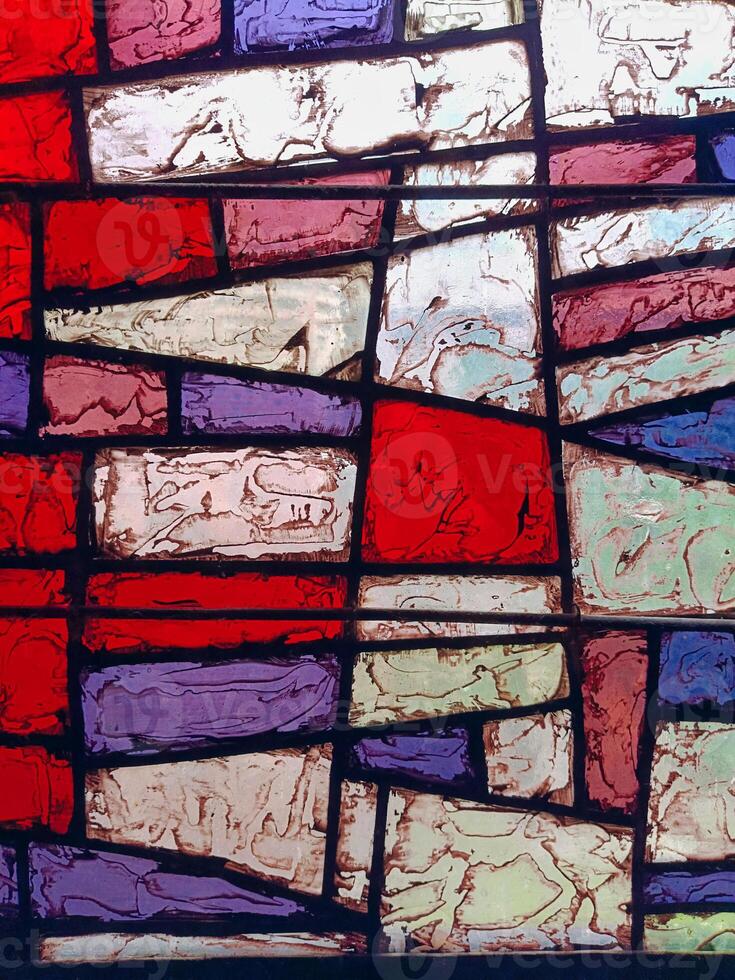 Close-up of abstract stained glass window with irregular colorful panels in red, purple, blue, and green. Textured surfaces and bold lines create artistic depth. Suitable for design, architecture photo