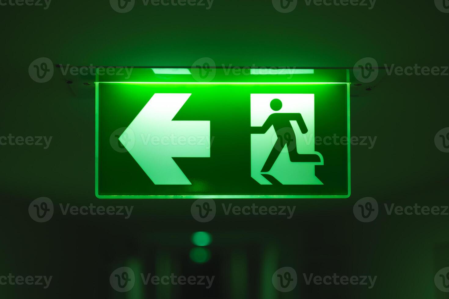 Exit way arrow direction guidance sign green color light emergency exit sign in a dark room photo