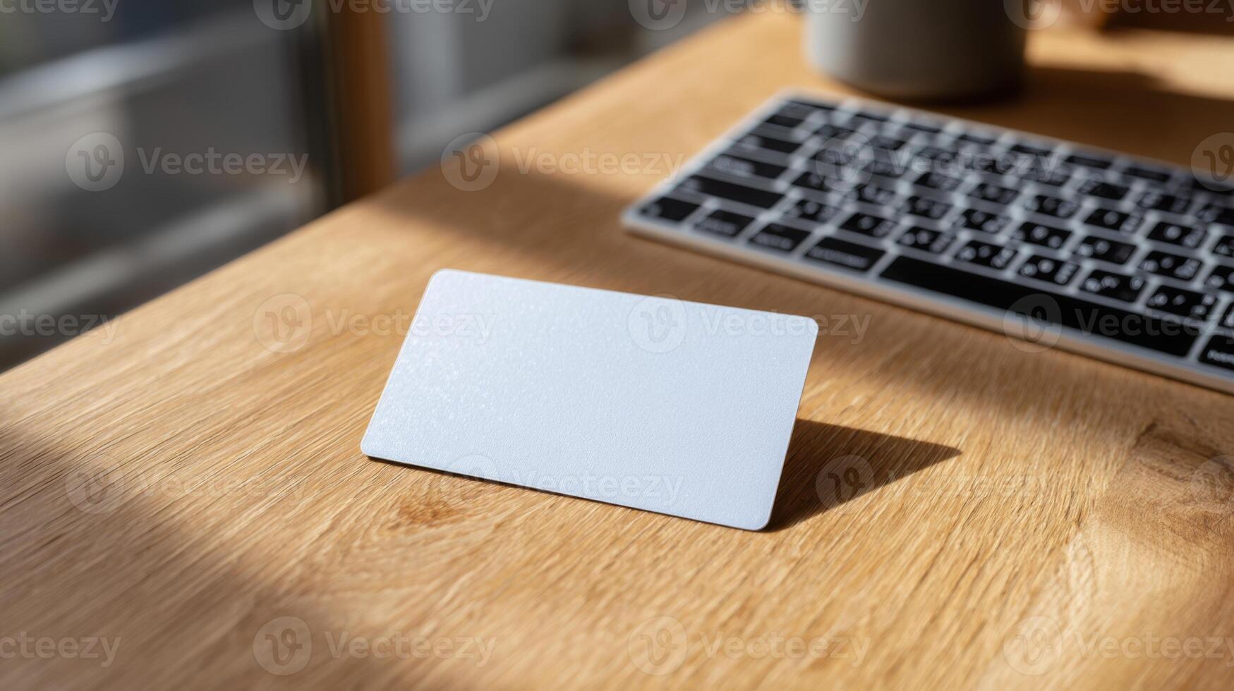 A blank business card on a wooden desk beside a keyboard, illuminated by soft natural light, creating a professional ambiance. photo