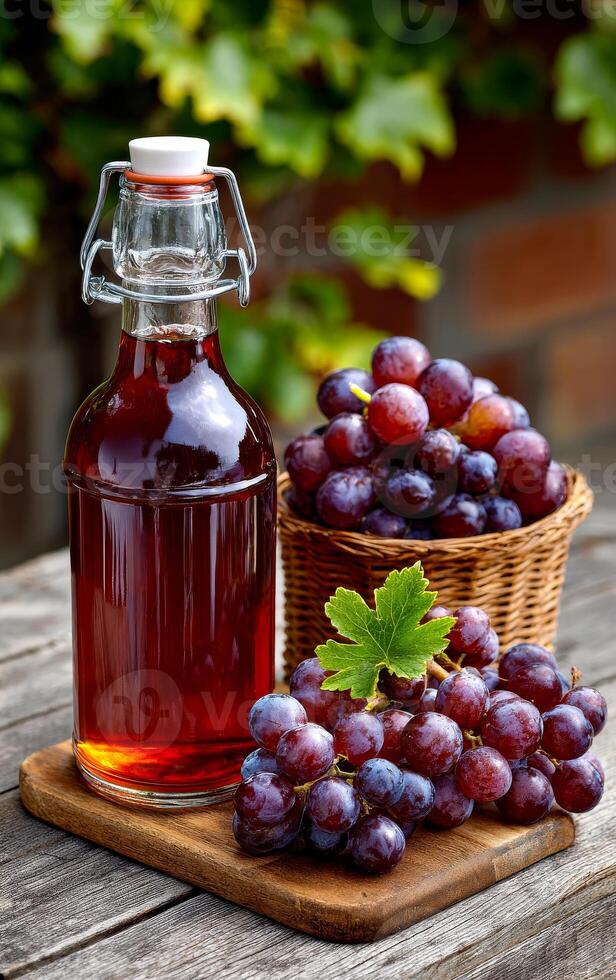 Fresh grape juice on wood. Grapes and a bottle of freshly pressed grape juice rest on a rustic wooden table surrounded by lush greenery. photo