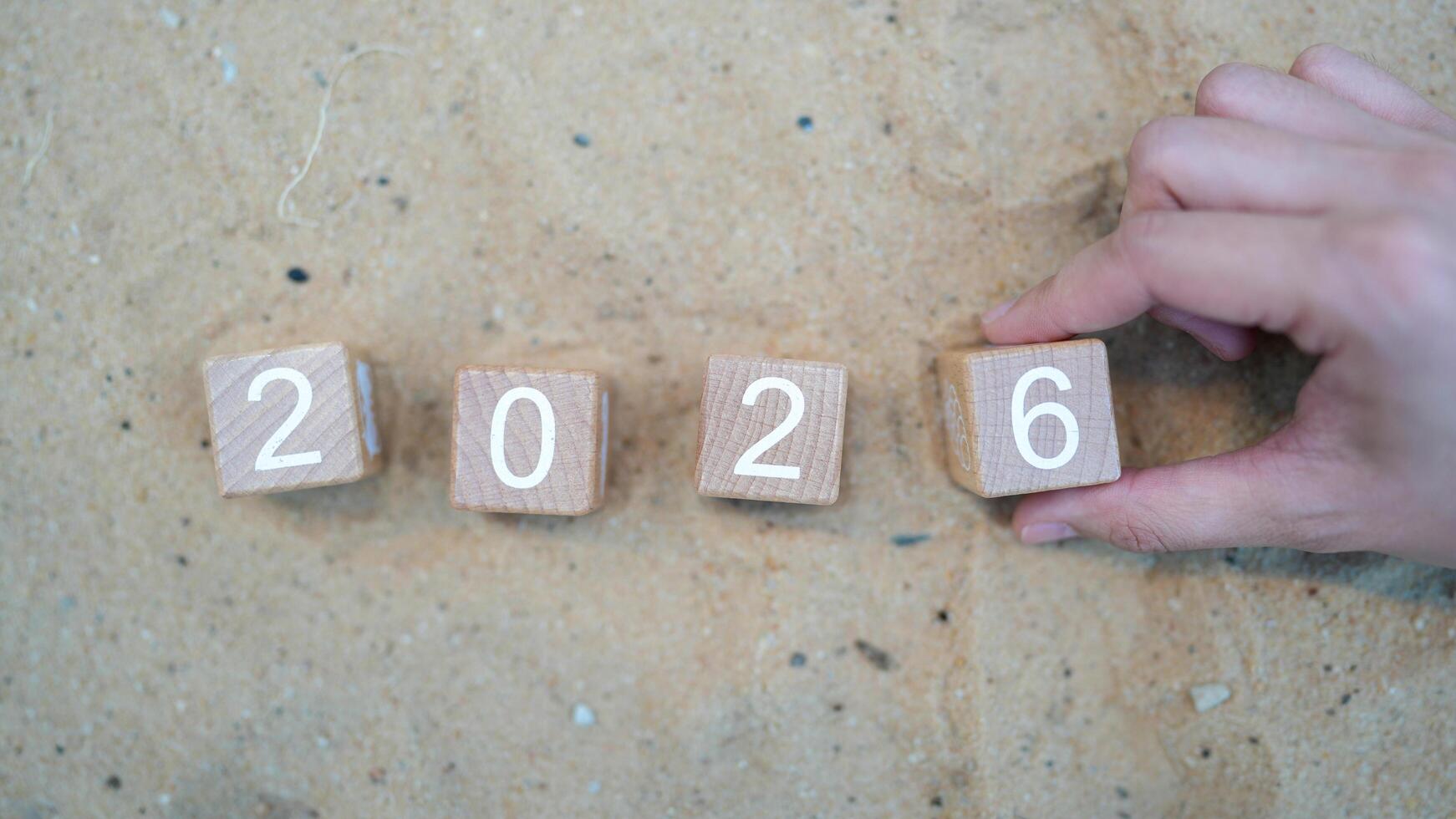Hand Placing Wooden Blocks Showing Number 2026 on Sandy Background for Concept of Future Year and Progress in Time Management and Planning photo